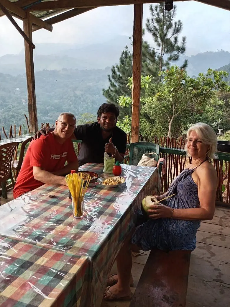 Dinu and two guests at a table with a view over the hills