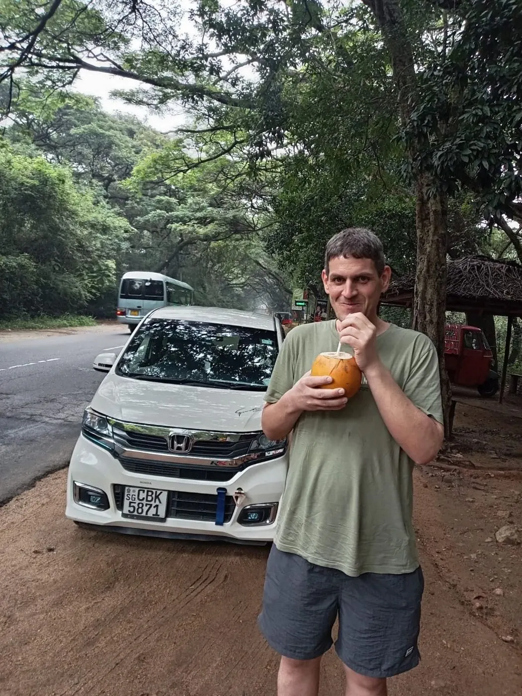 A guest drinking from a fresh coconut next to Dinu's car